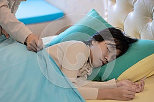 Asian child girl is sleeping on a bed in bedroom,mother putting up the blanket on her beautiful daughter,spending time together at