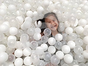 Asian child girl is smiling while lying in white balls at the playground.