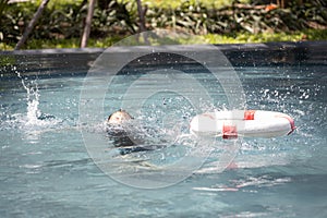 Asian child girl struggling for a life buoy in swimming pool to rescue drowning in dangerous situation in summer vacation,