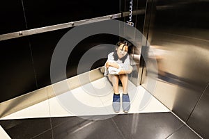 Asian child girl is stuck in an elevator,sad teenager girl sitting alone is crying in a despair with claustrophobia in elevator,