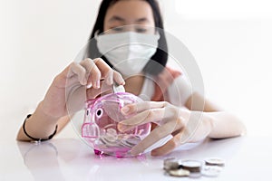 Asian child girl wear protective mask,put coin through the hole in piggy bank,try to save up more money for health care cost,