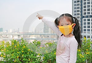 Asian child girl wearing a protection mask against PM 2.5 air pollution with pointing up in Bangkok city. Thailand