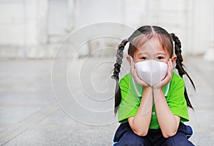 Asian child girl wearing a protection mask while outside to against PM 2.5 air pollution with pointing up in Bangkok city.