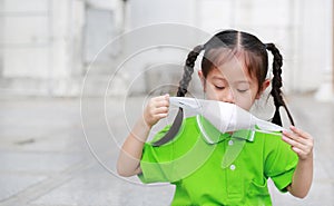 Asian child girl wearing a protection mask while outside to against PM 2.5 air pollution with pointing up in Bangkok city.