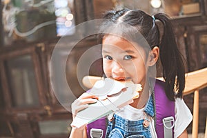 Asian child girls with backpack eating pancake after school in the school