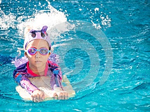 Asian child or kid girl wearing swimming suit to learning on swimming pool , learn and training swim on kick board