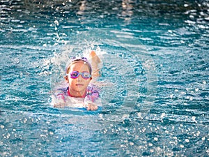 Asian child or kid girl wearing swimming suit to learning on swimming pool , learn and training swim on kick board