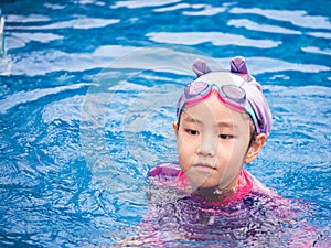 Asian child or kid girl wearing swimming suit to learning on swimming pool , learn and training swim on kick board