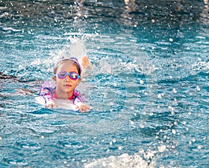 Asian child or kid girl wearing swimming suit to learning on swimming pool , learn and training swim on kick board