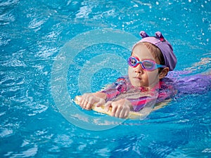 Asian child or kid girl wearing swimming suit to learning on swimming pool , learn and training swim on kick board