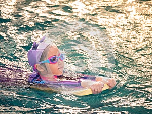 Asian child or kid girl wearing swimming suit to learning on swimming pool , learn and training swim on kick board