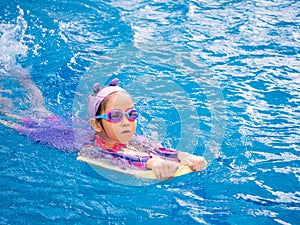 Asian child or kid girl wearing swimming suit to learning on swimming pool , learn and training swim on kick board