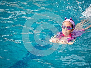 Asian child or kid girl wearing swimming suit to learning on swimming pool , learn and training swim on kick board