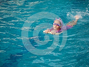 Asian child or kid girl wearing swimming suit to learning on swimming pool , learn and training swim on kick board