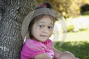 Asian child leaning on a tree