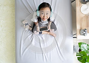 Asian child little girl play smartphone with wearing headphones on the bed