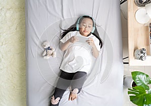 Asian child little girl play smartphone with wearing headphones on the bed