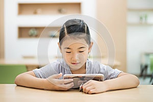 Asian child looking at smartphone at library desk.