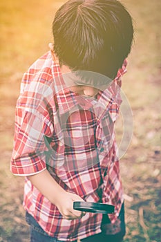 Asian child with magnifying glass at park on vacation. Education