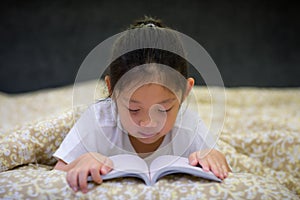 Asian Child Reading Book in Bed