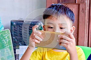 Asian child with squint eyes playing mobile game with smartphone. Concept of eye strain and screen addiction