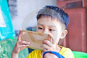 Asian child with squint eyes playing mobile game with smartphone. Concept of eye strain and screen addiction
