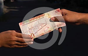 Asian children hand with 100 Riyal, the currency of Saudi Arabia, concept of giving. Selected focus and on dark background