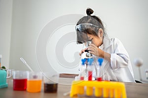 Asian children in lab coat using a microscope for a science experiment in homeschool laboratory