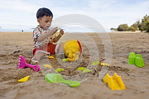 An Asian Chinese baby boy on the beach in the toys for the sand.