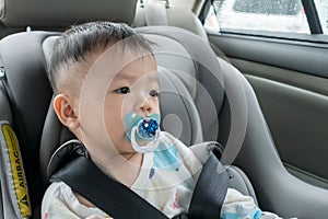Asian Chinese baby boy with emotion face and sucking pacifier while sit on child safety car seat