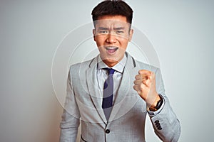 Asian chinese businessman wearing grey jacket and tie standing over isolated white background angry and mad raising fist