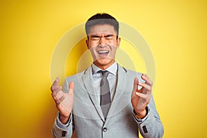 Asian chinese businessman wearing suit and tie standing over isolated yellow background celebrating mad and crazy for success with