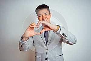 Asian chinese businessman wearing suit and tie standing over isolated yellow background smiling in love doing heart symbol shape