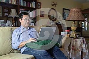 Asian Chinese businessman working on his laptop in his house living hall. Work from home concept