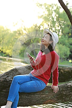 Asian Chinese careless girl is listening to music sit on a tree by a river in spring autumn park
