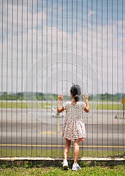 Asian chinese girl child looking at luxury jets from behind the gates of airport