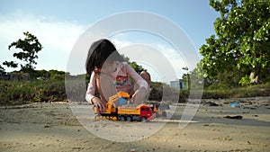 Asian chinese girl child playing with earth mover toys by the beach