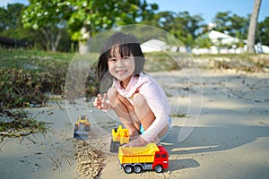 Asian chinese girl child playing with soil mover toys by the beach