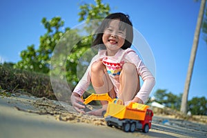 Asian chinese girl child playing with soil mover toys by the beach
