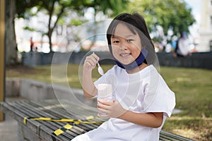 Asian Chinese girl child taking mask off and enjoying ice cream outdoors