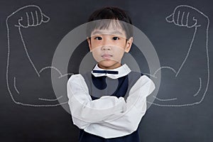 Asian Chinese girl standing against blackboard with sketched strong arms