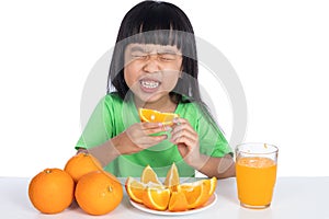 Asian Chinese little girl eating sour orange and making grimace photo