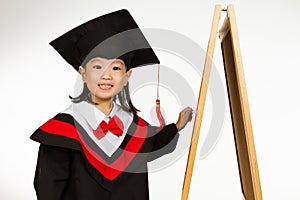 Asian Chinese little girl in graduation gown againts blackboard