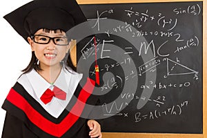 Asian Chinese little girl in graduation gown againts blackboard