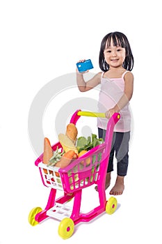 Asian Chinese little girl holding credit card with shopping trolley full of vegetables
