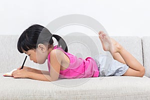 Asian Chinese little girl laying on the sofa writting book photo