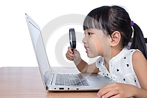 Asian Chinese little girl looking at laptop through magnifier