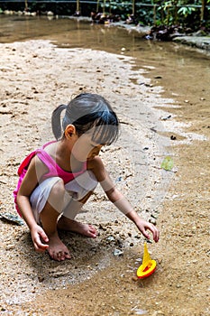 Asian Chinese little girl playing toy boat at creek