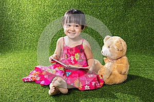 Asian Chinese little girl reading book with teddy bear