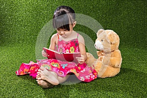 Asian Chinese little girl reading book with teddy bear